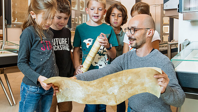 Eine Kindergruppe betrachtet im Rahmen einer Führung ein Stück Pergament.